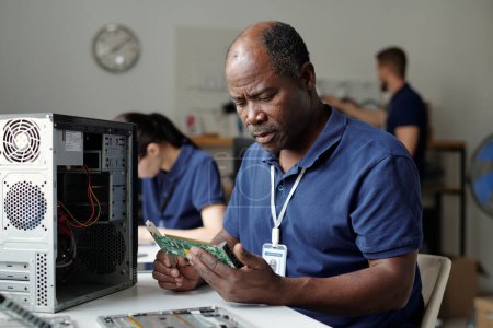 Photo for Experienced technician or worker of repair service office looking at computer motherboard while checking parts of processor - Royalty Free Image