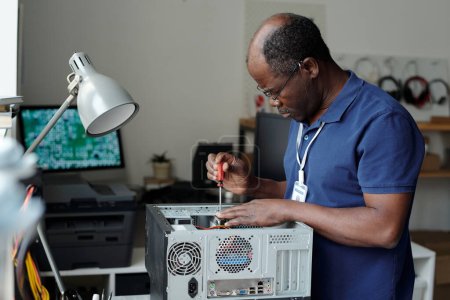 Seitenansicht eines erfahrenen Technikers mit einem Schraubenzieher in der Hand, der Details der Computerhardware fixiert, während er am Arbeitsplatz steht