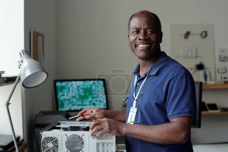 Erfahrener afroamerikanischer Reparateur im blauen Hemd schaut lächelnd in die Kamera, während er den Computerprozessor überprüft und repariert