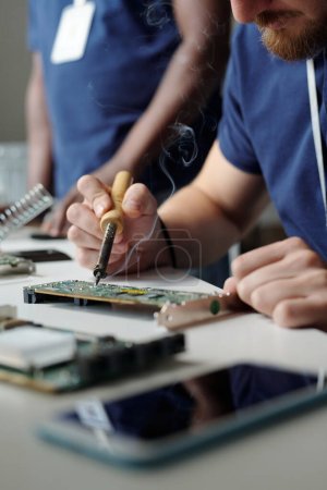 Foto de Primer plano del joven técnico del servicio de mantenimiento utilizando una herramienta eléctrica mientras se repara parte del procesador informático por lugar de trabajo - Imagen libre de derechos