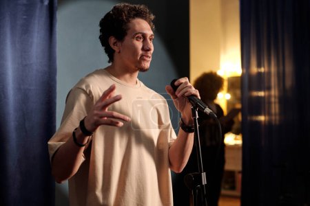 Jeune acteur ou comédien avec microphone debout sur scène devant le public et prononçant un monologue pendant la représentation