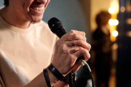 Hands of young stand up comedian holding microphone and speaking to audience while standing in front of camera during performance