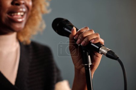 Mano de joven alegre hembra de pie comediante sosteniendo micrófono y pronunciando monólogo mientras está de pie delante de la cámara