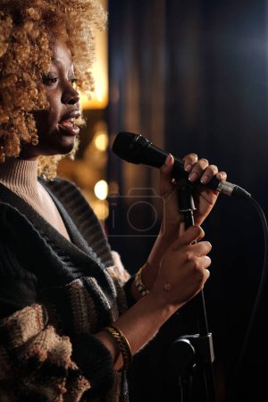 African American female comedian with microphone standing on stage in front of audience while presenting them new monologue