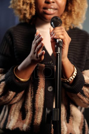 Micrófono en manos de una joven comediante o presentadora afroamericana que pronuncia monólogo o habla con el público