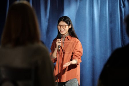 Téléchargez les photos : Joyeux jeune participante de stand up show prononçant monologue dans le microphone et en regardant le public - en image libre de droit