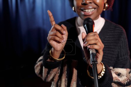 Foto de Micrófono sostenido por el joven comediante afroamericano de stand up show pronunciando monólogo mientras está de pie en el escenario - Imagen libre de derechos