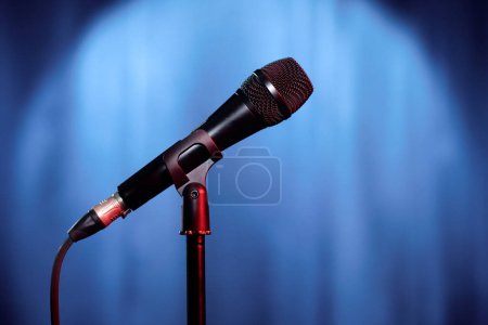 Téléchargez les photos : Microphone du présentateur ou participant du spectacle du soir debout sur scène avec des rideaux bleus éclairés par la lumière du réflecteur avant la performance - en image libre de droit