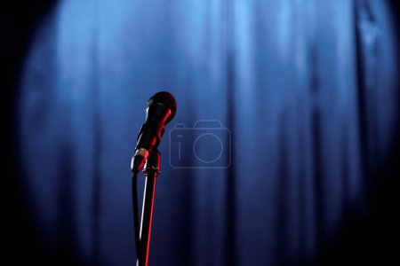 Téléchargez les photos : Microphone préparé pour le comédien du stand up club ou participant à un spectacle populaire en soirée debout sur scène avec des rideaux bleus - en image libre de droit