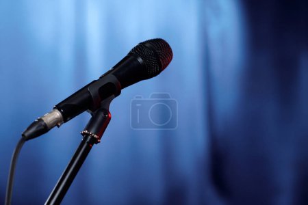 Foto de Micrófono de comediante de stand up club o persona invitada para el popular espectáculo nocturno de pie en el escenario contra cortinas azules - Imagen libre de derechos