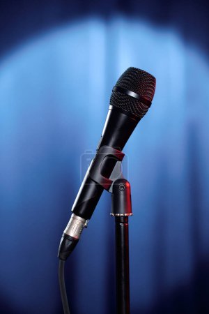 Photo for Microphone of participant of evening show or actor having rehearsal standing in front of camera on stage with blue curtains - Royalty Free Image