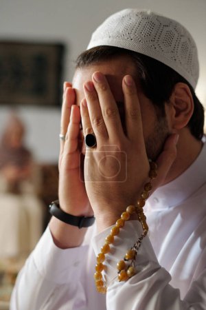 Vertikale Nahaufnahme eines bis zur Unkenntlichkeit bekleideten muslimischen Mannes, der eine Taqiyah trägt und einen Salah betet