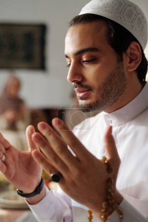 Vertikale Nahaufnahme eines jungen Mannes aus dem Nahen Osten, der weiße Kandora und Taqiyah-Salat mit Misbaha in der Hand trägt