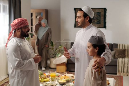 Foto de Hombre maduro de Oriente Medio hablando con su hermano menor y sobrino en la reunión familiar en el día de Eid Al-Fitr - Imagen libre de derechos
