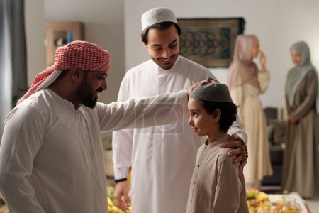 Téléchargez les photos : Joyeux barbu Moyen-Orient tapotant son neveu sur la tête à la réunion de famille sur Uraza Bayram jour - en image libre de droit