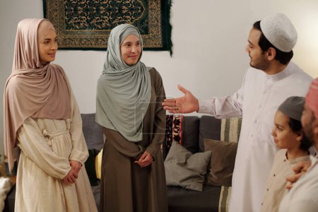 Téléchargez les photos : Plan à moyen terme d'hommes, de femmes et d'enfants musulmans modernes debout dans le salon lors d'une réunion de famille le jour d'Uraza Bayram - en image libre de droit