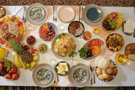 Foto de Tiro plano de arriba hacia abajo de abundante mesa festiva servida con platos caseros, verduras, frutas y aperitivos para la celebración de Eid Al-Fitr - Imagen libre de derechos