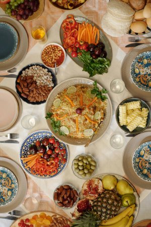 Vertical flat lay no people shot of pilaf, vegetables, fruits and snacks on festive table on Uraza Bayram day