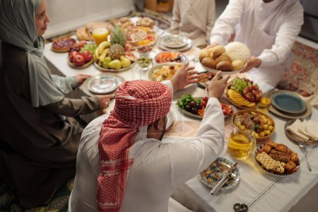 Téléchargez les photos : Vue panoramique du jeune homme musulman partageant sa nourriture avec sa famille lors d'un dîner festif sur Uraza Bayram - en image libre de droit