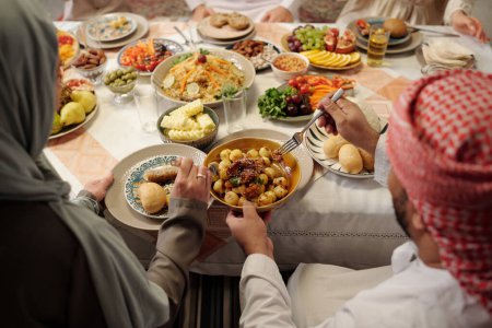 Téléchargez les photos : Vue en angle élevé au-dessus de la photo d'un homme musulman méconnaissable partageant un délicieux plat de pommes de terre avec sa femme lors d'un dîner en famille sur Uraza Bayram - en image libre de droit