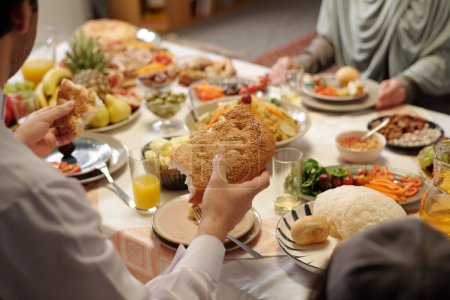 Téléchargez les photos : Homme musulman méconnaissable dîner festif avec sa famille prendre un morceau de pain plat sur Uraza Bayram, espace de copie - en image libre de droit