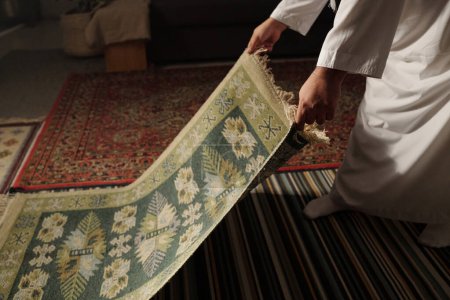 Foto de Hombre musulmán irreconocible colocando alfombra de oración en el suelo en la sala de estar en casa antes de namaz, espacio de copia - Imagen libre de derechos