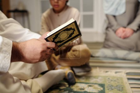 Téléchargez les photos : Gros plan sélectif d'un musulman méconnaissable lisant la sourate du Coran lors d'un rassemblement familial à la maison, espace de copie - en image libre de droit