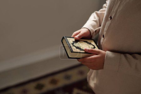 Téléchargez les photos : Vue en angle élevé d'un enfant méconnaissable tenant un livre saint du Coran dans les mains, espace de copie - en image libre de droit