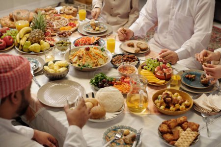 Foto de Gran angular de la irreconocible familia musulmana sentada en la abundante mesa festiva celebrando Eid Al-Fitr, espacio para copiar - Imagen libre de derechos