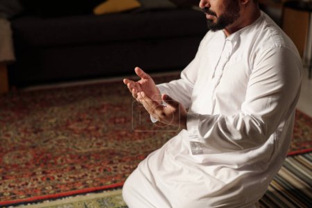 Foto de Vista de ángulo alto de hombre musulmán barbudo en ropa blanca sentado en la alfombra rezando salah, espacio de copia - Imagen libre de derechos