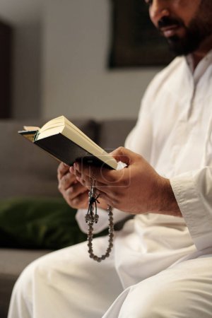 Téléchargez les photos : Mise au point sélective verticale d'un homme barbu du Moyen-Orient tenant un misbaha lisant un livre du Coran - en image libre de droit