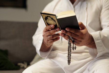 Foto de Medio primer plano de las manos de un musulmán irreconocible sosteniendo misbaha leyendo el libro del Corán - Imagen libre de derechos