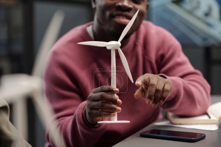 Schnappschuss eines jungen erfolgreichen afroamerikanischen Geschäftsmannes, der das Modell einer Windmühle berührt, während er sein Geschäftsprojekt vorstellt