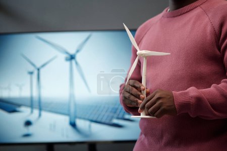 Téléchargez les photos : Modèle de moulin à vent entre les mains d'un jeune employé afro-américain en pull décontracté debout contre un tableau interactif lors d'une conférence - en image libre de droit