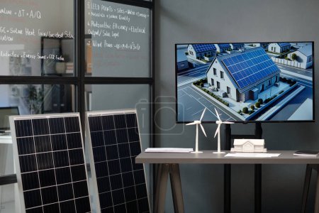 Workplace of modern architect with visual template of new residence with solar panels on interactive board and windmill models on desk
