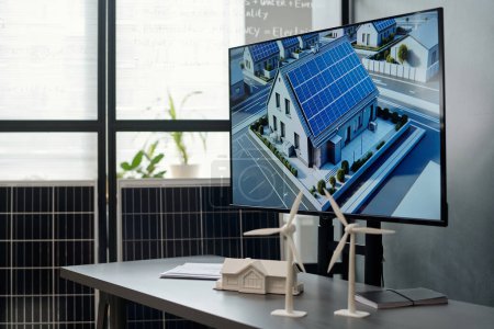 Photo for Models of windmills and house on desk with visual template of new residence with solar panels on interactive board in office - Royalty Free Image