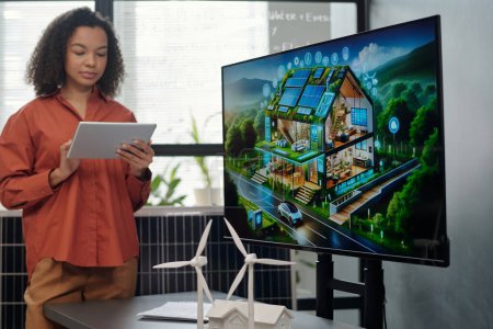 Photo for Screen with new architectural project and two models of windmill standing on desk against young female employee making presentation - Royalty Free Image
