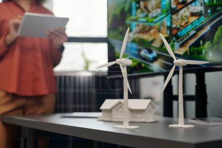 Foto de Dos modelos de molino de viento de pie en escritorio gris junto a la maqueta de la casa de plástico y tablero interactivo con plantilla visual de nuevo proyecto empresarial - Imagen libre de derechos