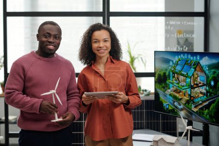 Foto de Dos jóvenes y felices empleados afroamericanos con tableta y molino de viento mirando a la cámara mientras se preparan para la presentación - Imagen libre de derechos