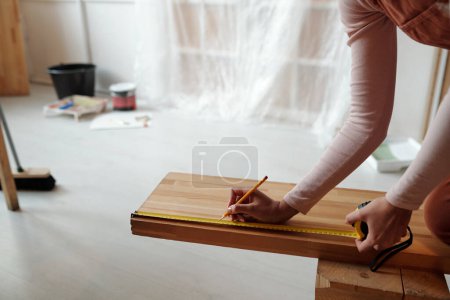 Photo for Cropped shot of young female worker taking measures of wooden bench against interior of new cafe with unfinished renovation - Royalty Free Image