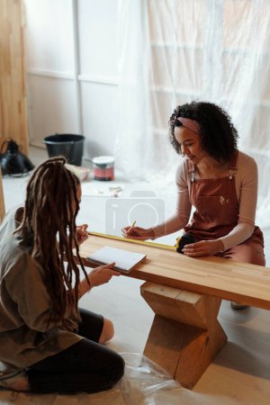 Foto de Dos jóvenes diseñadores o empresarios sentados en la cafetería y tomando medidas de banco de madera mientras hacen trabajos de renovación - Imagen libre de derechos