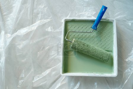 Photo for Top view of plastic tray with paintroller and green paint standing on the floor covered with cellophane and prepared for renovation work - Royalty Free Image