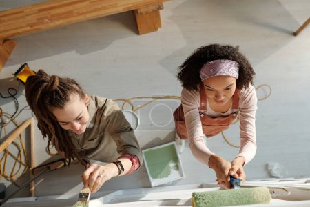 Téléchargez les photos : Vue ci-dessus de deux jeunes femmes interculturelles avec peintre et peinture au pinceau mur de café en vert pendant la rénovation - en image libre de droit