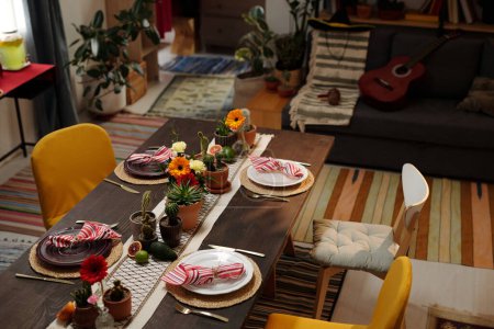 Foto de Varias sillas alrededor servían mesa con flores domésticas, frutas exóticas y platos con servilletas de pie delante de la cámara - Imagen libre de derechos