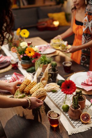 Téléchargez les photos : Mains de jeune femme avec bracelet sur le poignet plateau de mise avec du maïs cuit sur la table de fête servi pour les amis et autres invités - en image libre de droit