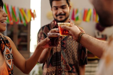 Téléchargez les photos : Mains de jeunes amis heureux cliquetis avec des verres de tequila pendant la célébration du Cinco de mayo tout en appréciant la fête à la maison - en image libre de droit