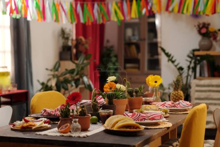 Tasty homemade snacks and other treats standing on served festive table decorated by domestic flowers growing in flowerpots