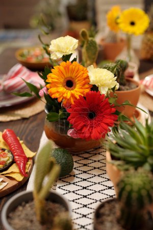 Bunch of red, white and orange color flowers in the center of served table next to homemade snacks and other treats prepared for guests