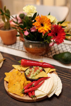 Foto de Aperitivos apetitosos sobre tabla de madera de pie sobre mesa festiva decorada con racimo de gerberas frescas y claveles y cactus en macetas - Imagen libre de derechos