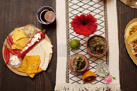 Top view of wooden table served with appetizing homemade snacks, glass of tequila, citrus fruits and flowers prepared for celebrating holiday